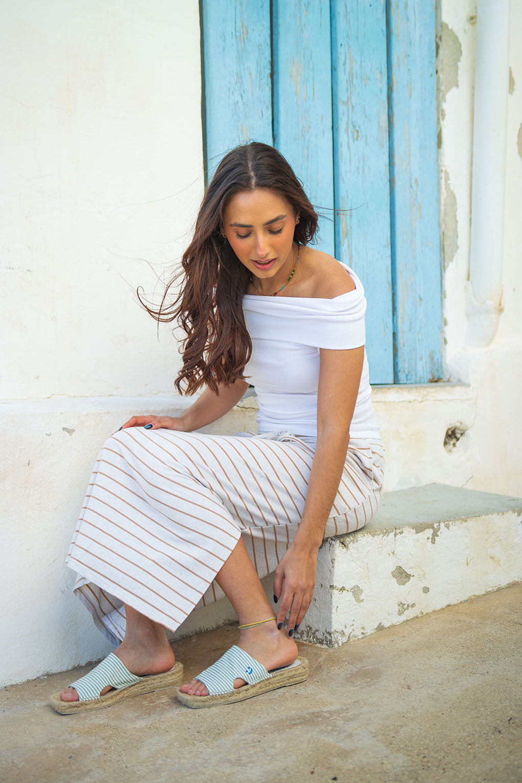 Modelo sentada en una fachada mediterránea de barraca valenciana con las sandalias con suela de yute natural Lloret Amande de MYBARKS. Las alpargatas de mujer de mybarks son cosidas a mano en España con materiales sostenibles. 