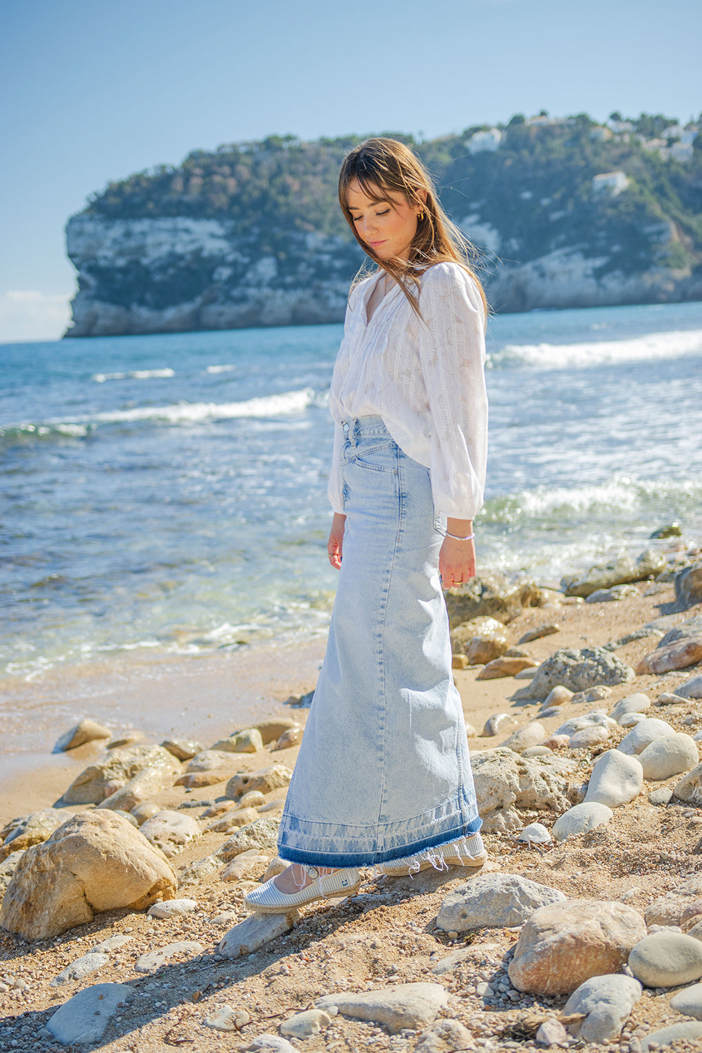 Modelo frente al mar llevando unas merceditas con suela de yute natural cosidas a mano en España en color azul cielo. Las alpargatas Valetta Cielo son un modelo a rayas con aroma a cítricos. 