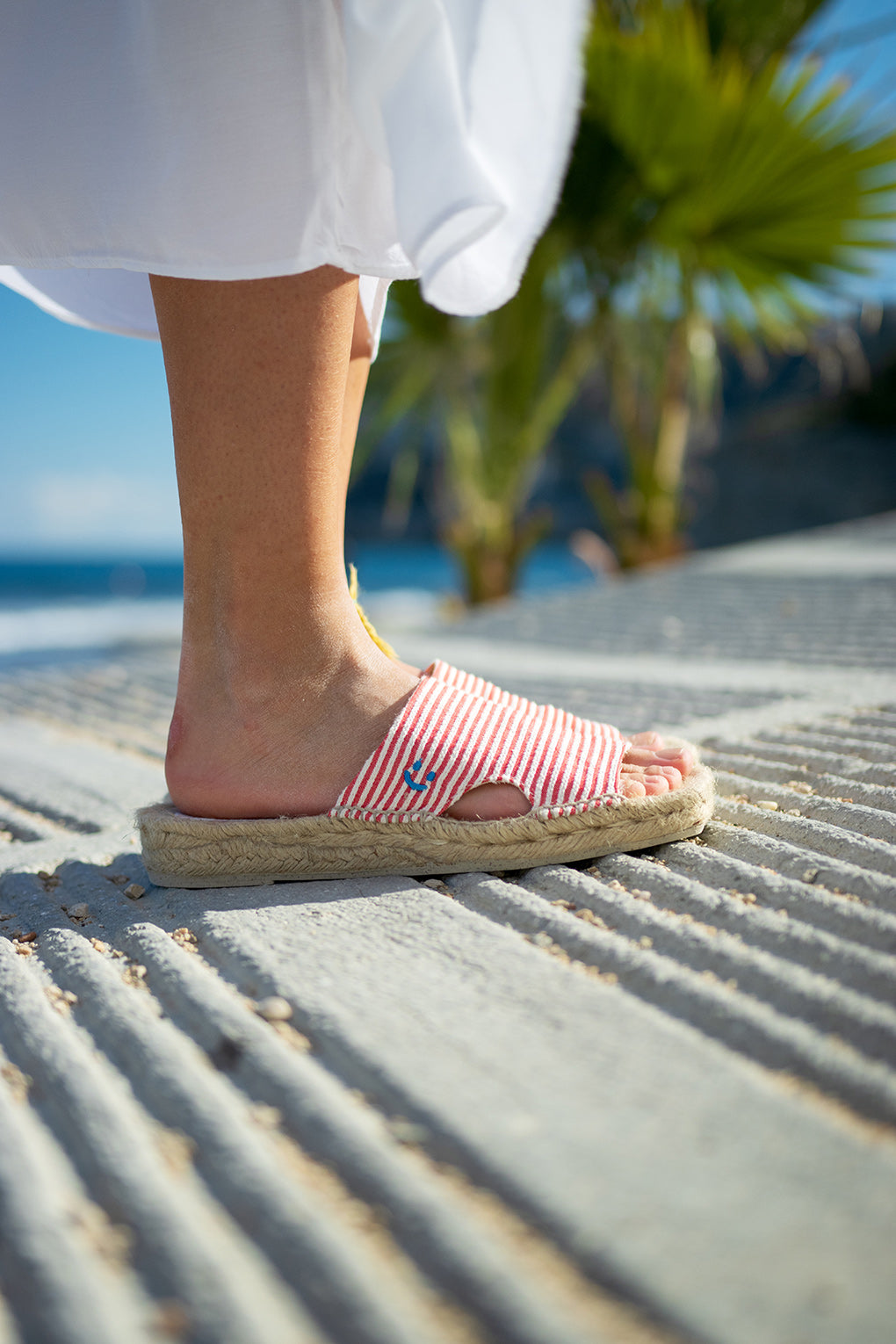 Detalle con el mar Mediterráneo de fondo de las alpargatas Lloret Cereza de MYBARKS. Unas sandalias para mujer a rayas hechas a mano en España con materiales sostenibles y aroma a cítricos. 