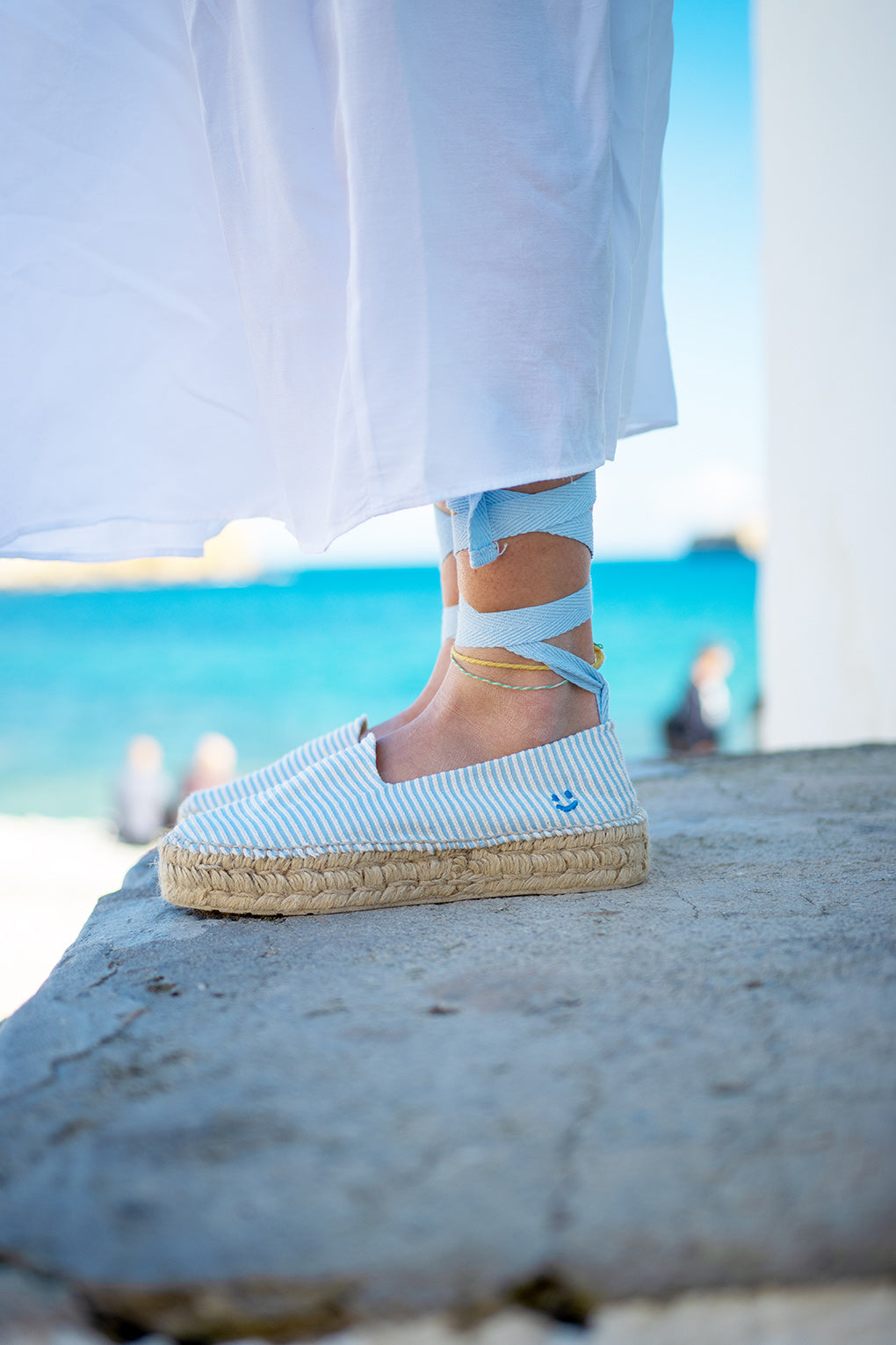 Imagen detalle de las alpargatas para mujer Roses Cielo de MYBARKS sobre el mar de fondo.  Estas alpargatas con una cinta de lino que se ata al pie son perfectas para un look sofisticado y veraniego. 